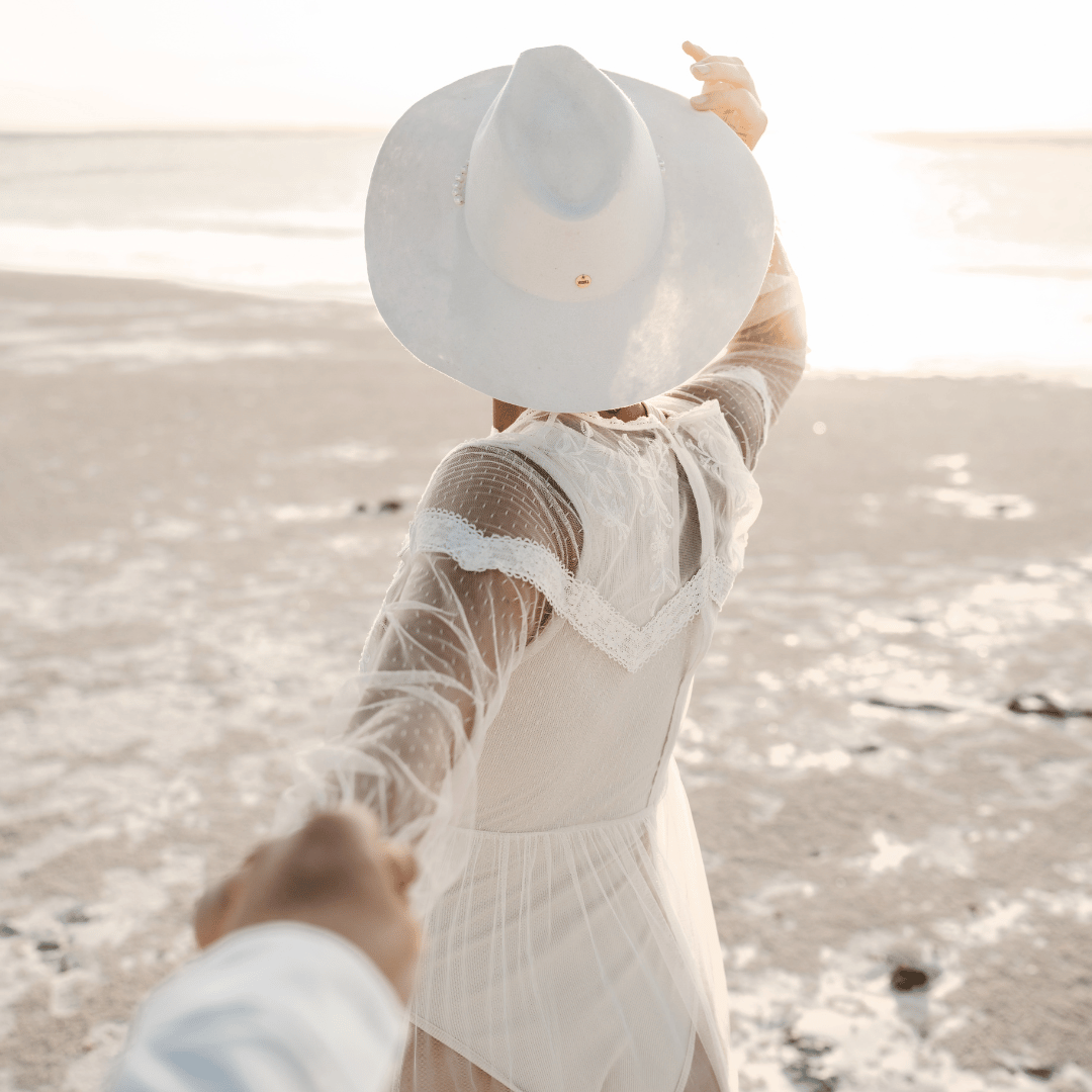 Novia - Fedora Braut Hut - weißer Fedora Hochzeitshut für Damen- Fedora mit breiter und steifer Krempe - Model mit Fedora Brauthut am Strand - Strandhochzeit - Nimanita Hats - Hüte für Frauen - Model von hinten.png