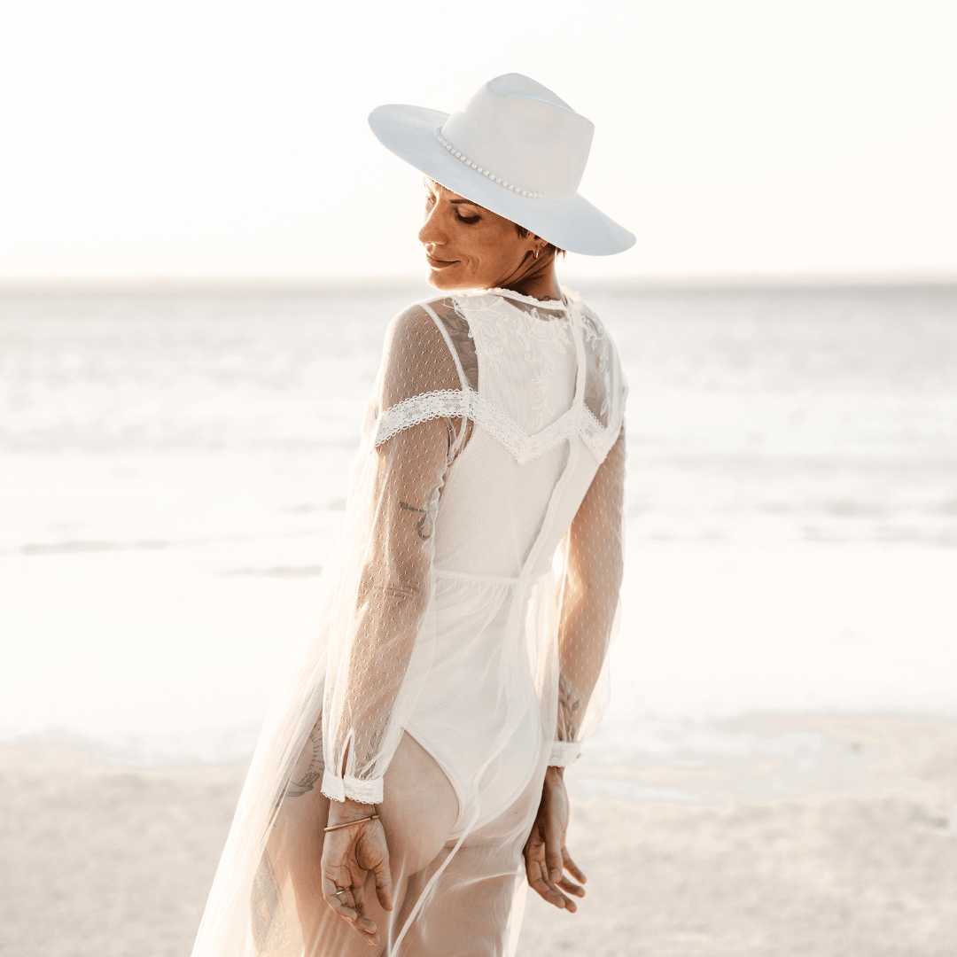 Novia - Fedora Braut Hut - weißer Fedora Hochzeitshut für Damen- Fedora mit breiter und steifer Krempe - Model mit Fedora Brauthut am Strand - Strandhochzeit - Nimanita Hats - Hüte für Frauen - Model von schräg hinten