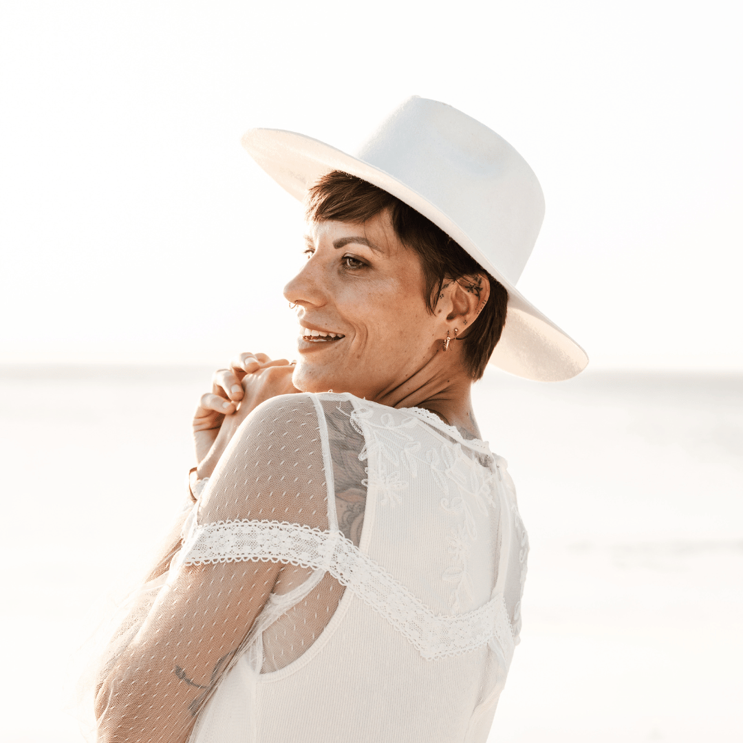 Novia - Fedora Braut Hut - weißer Fedora Hochzeitshut für Damen- Fedora mit breiter und steifer Krempe - Model mit Fedora Brauthut am Strand - Strandhochzeit - Nimanita Hats - Hüte für Frauen - Model von seite